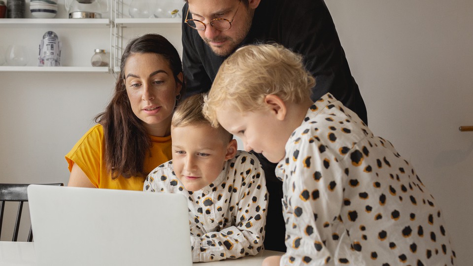 Familj med två föräldrar och två barn sitter tillsammans och tittar på en datorskärm