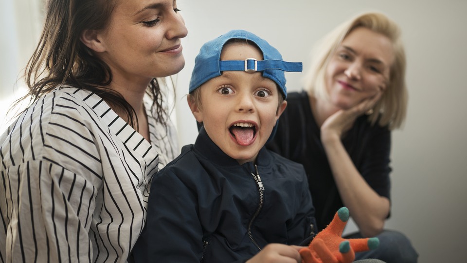 En mamma håller i sin son som sträcker ut tungan med en keps på huvudet. 