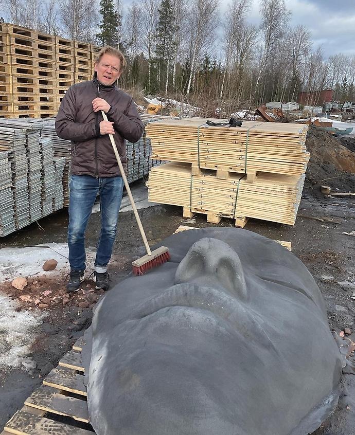 Konstnären Johan Ström vid den färdiggjutna skulpturen, ett liggande ansikte. Johan har en kvast i handen.