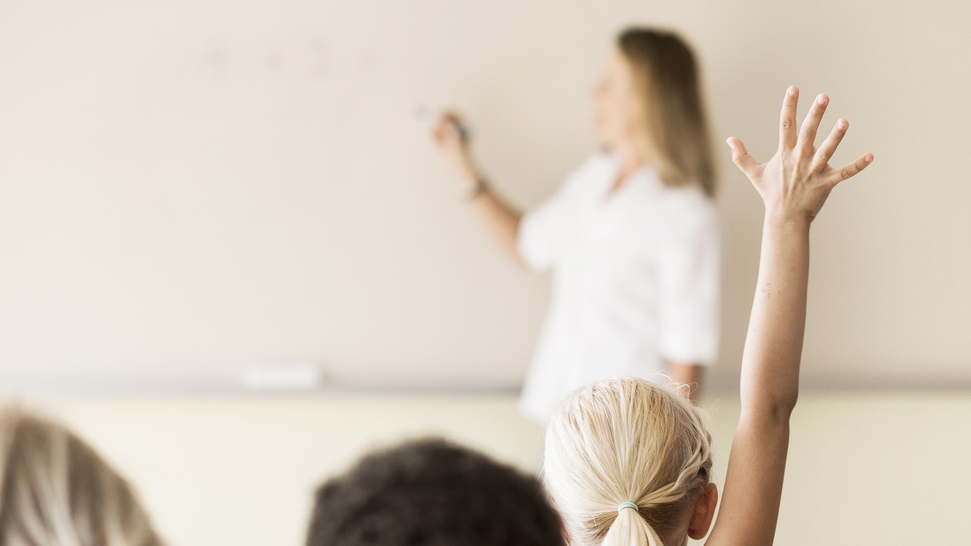 pedagog som skriver på tavlan och elev som räcker upp handen