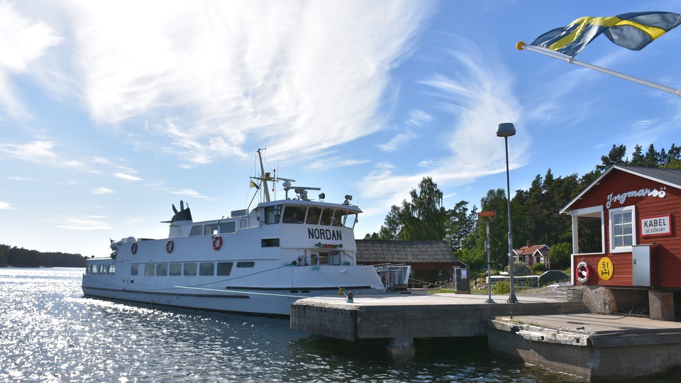 Brygga på Husarö med livboj och skärgårdsbåt som är på väg att lägga till.