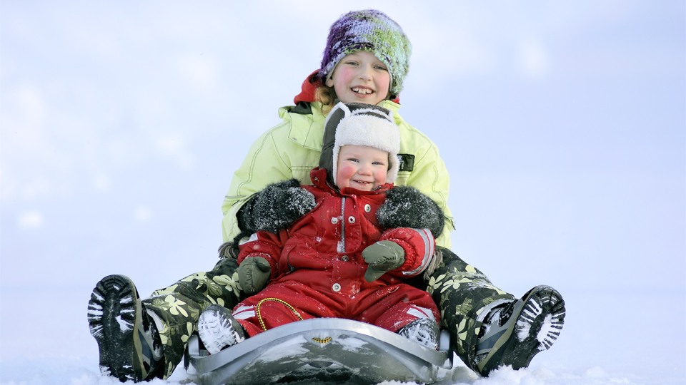 Två barn sitter i en pulka i snön. 