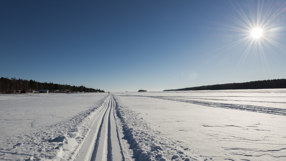 Preparerade skidspår på snöbelagd is. Vädret är soligt och himlen är klarblå.