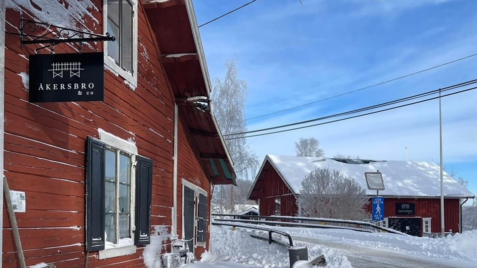 Bilden visar en faluröd träbyggnad med en svart skylt där det står Åkersbro & co.