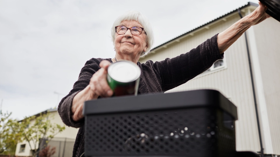 En kvinna lägger en metallburk i ett avfallskärl