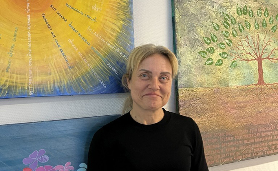 Gabriella Morell, enhetschef på Solskiftet barn och unga. Hon står framför tavlor målade av en av hennes medarbetare.