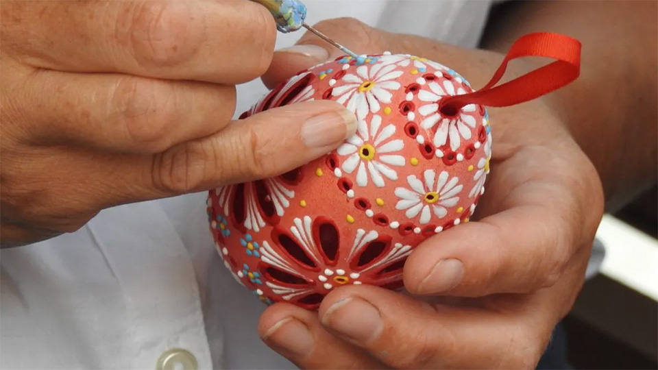 En närbild på ett par händer som håller i ett ägg. Det målas i vackra mönster.