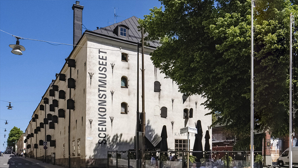 Ett stort stenhus på fyra våningar. Fönstren har rundade bågar och öppna fönsterluckor.