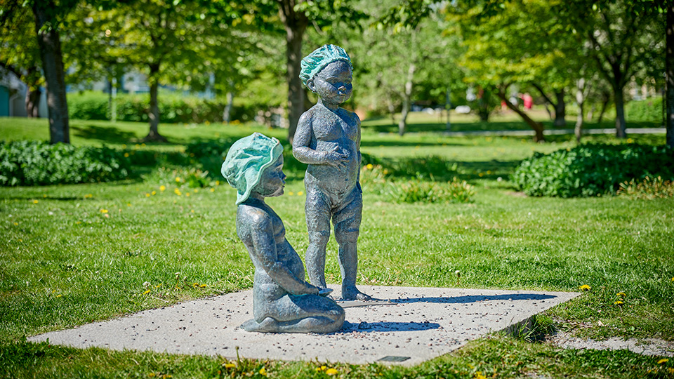 En skulptur av två små flickor med badmössor. Konstverket står utomhus på en gräsmatta.