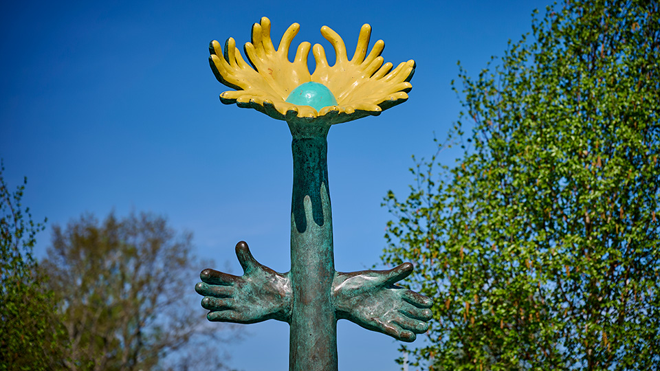 En hög solros i brons. Bladen under blomman ser ut som två händer.