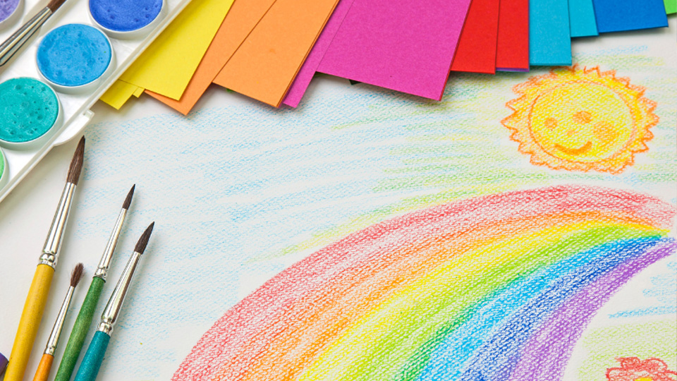 En regnbåge ritad med krita. På bordet finns också målarpenslar och färgglada papper.
