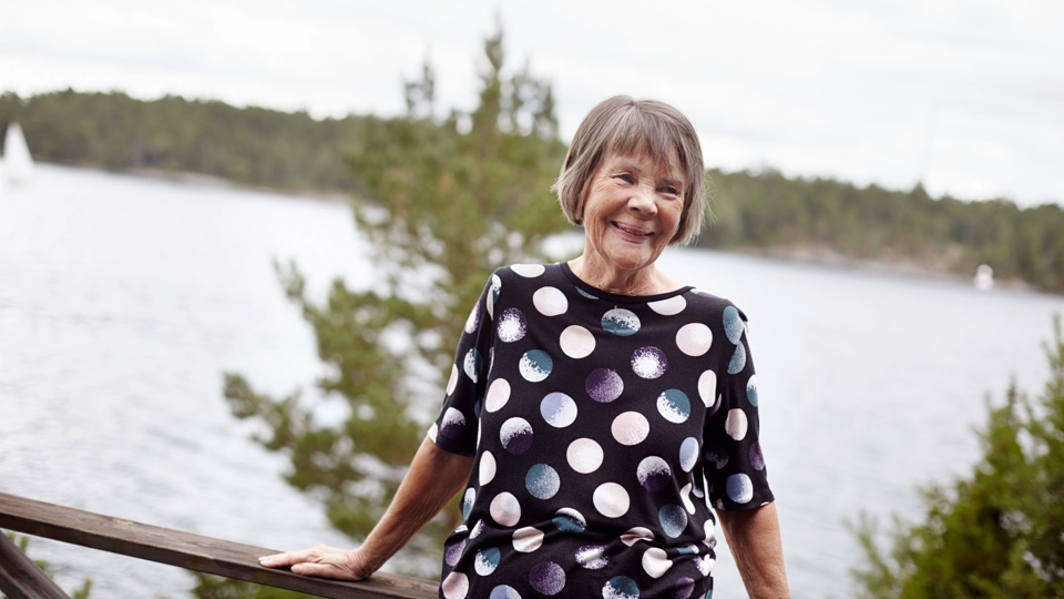 En kvinna står på en terrass med vatten i bakgrunden.