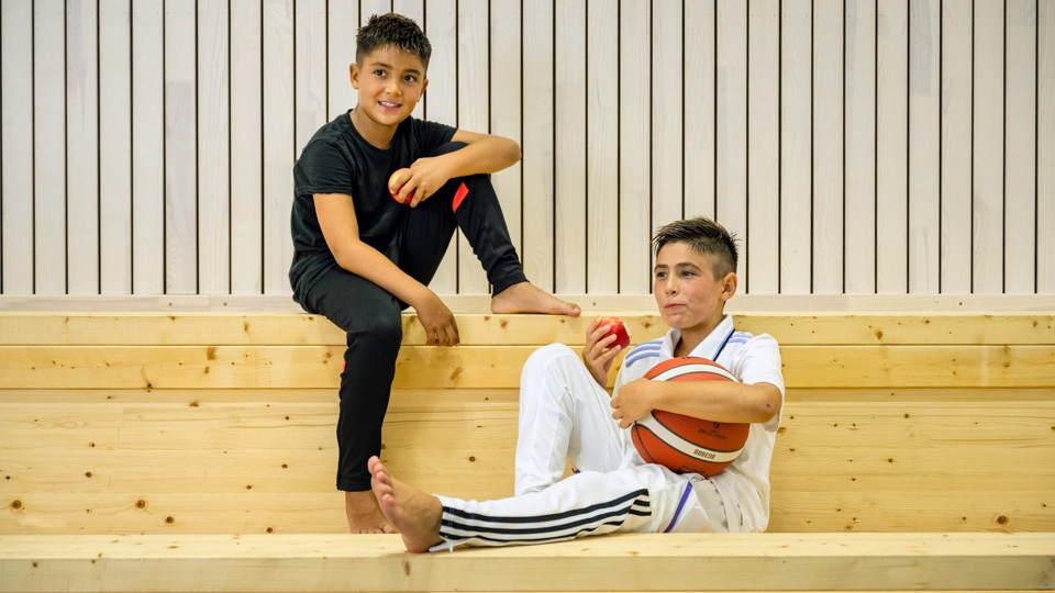 Två unga pojkar i träningskläder sitter på en läktare.