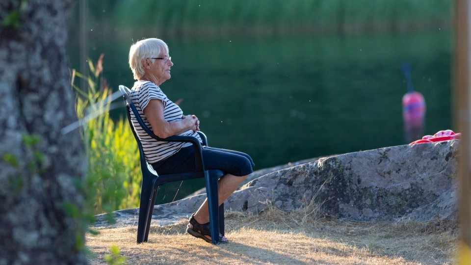 Nainen istuu iltavalaistuksessa tuolissa rannalla kivien ympäröimänä