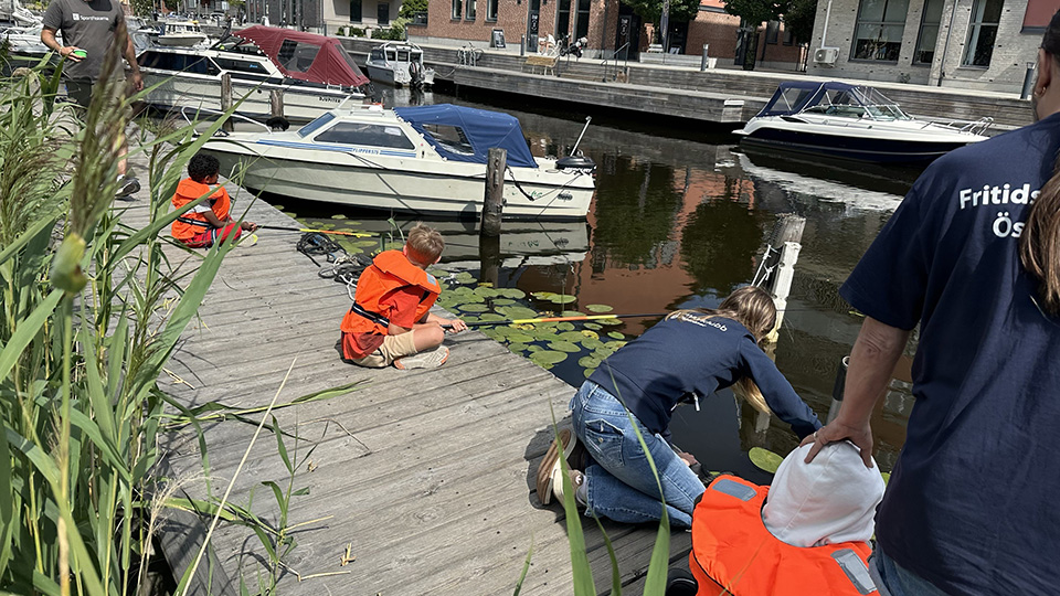 Två pojkar sitter med flytväst på piren vid Åkers kanal.