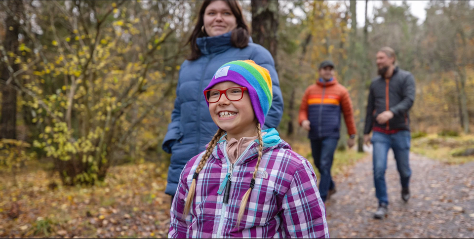 Tre vuxna och ett barn promenerar längs en stig i skogsmiljö