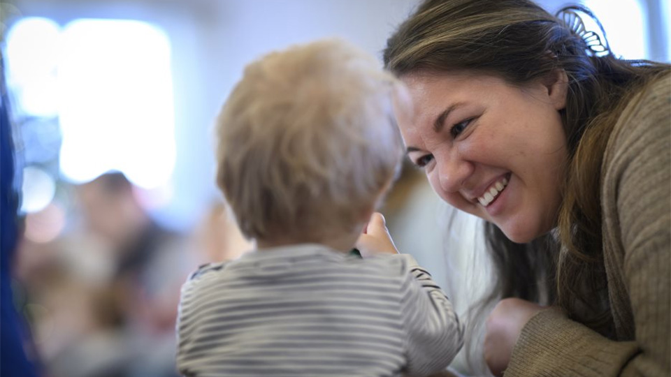 En kvinna ler stort mot en liten bebis.