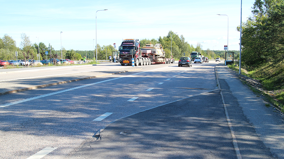En närbild på en trafikerad motorväg med en bilparkering på andra sidan vägen.
