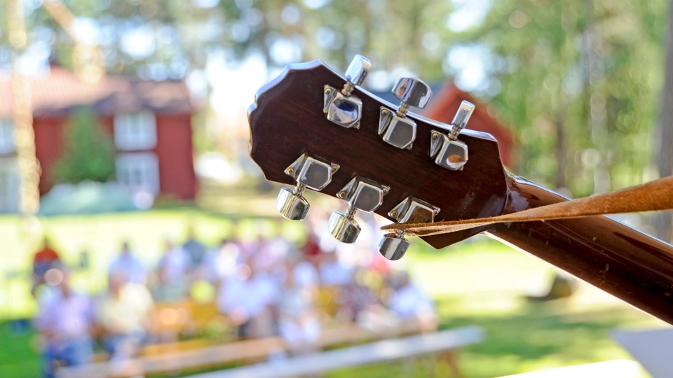 Närbild på gitarrhals sett från scen, med publik sittande nedanför i oskärpa i utemiljö sommartid