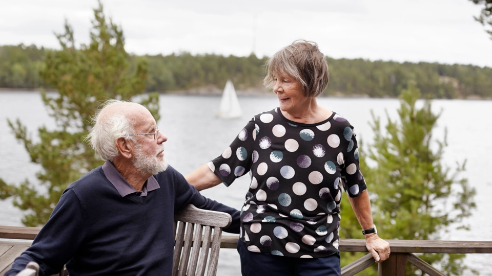 Äldre par på en terrass med vatten bakom.