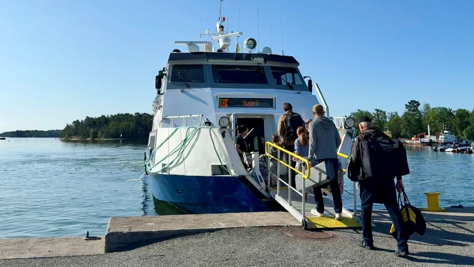 Människor går ombord på en mindre skärgårdsfärja. Platsen är Åsättra brygga på Ljusterö.