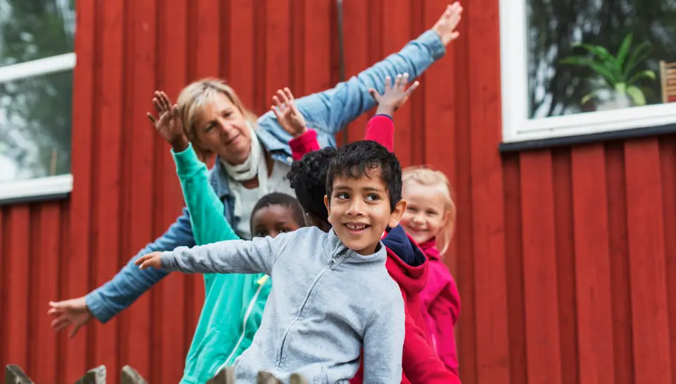 Förskolebarn ler och håller ut armarna tillsammans med en pedagog