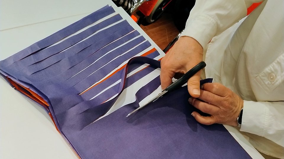 Lähikuva vappuviuhkan valmistuksesta: koristeellista paperia leikataan liuskoiksi