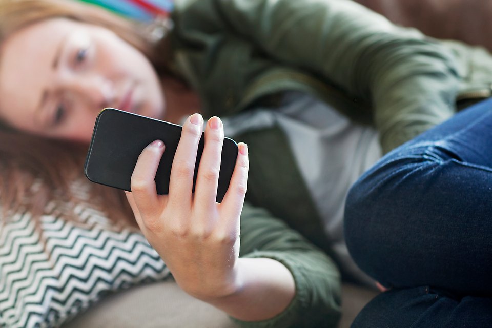 Ledsen ung tjej ihopkrupen på soffa med mobil i handen