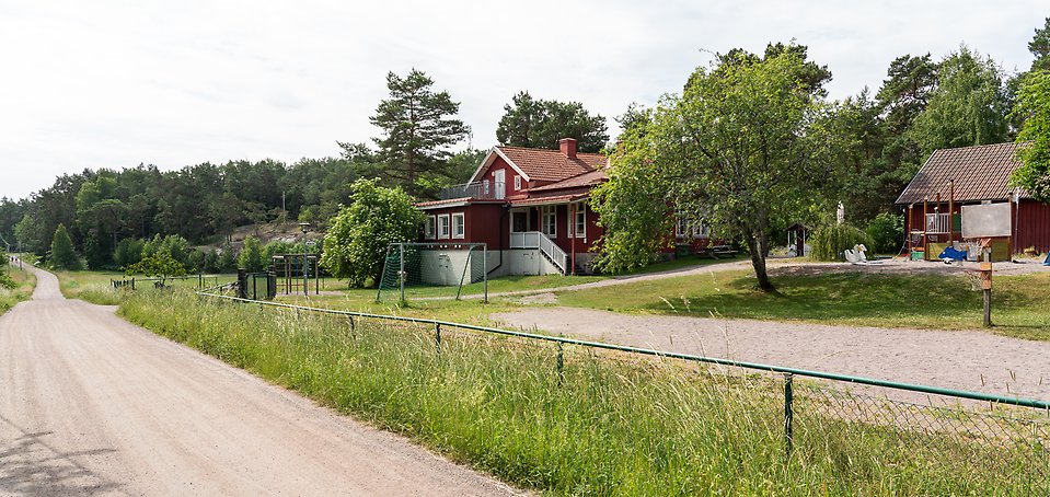 Ingmarsö pedagogiska omsorg, röd träbyggnad med grusväg framför. Stora grönområden runt byggnaden.
