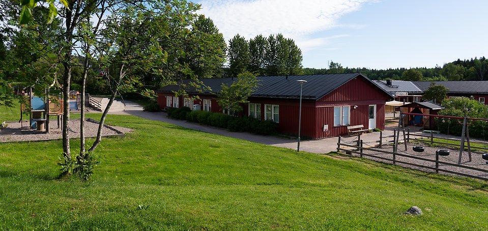 Kantarellens förskola, röd träbyggnad omgiven av gräs, gungor och lekplats 