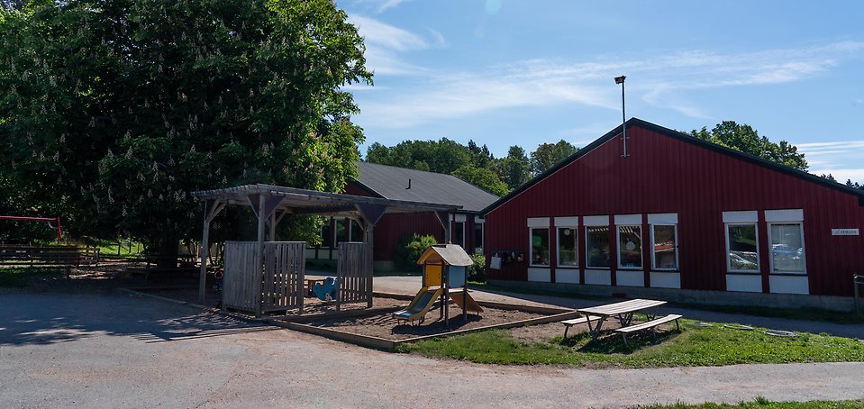 Luffarbackens förskola, röd träbyggnad med sandlåda och lekställning framför