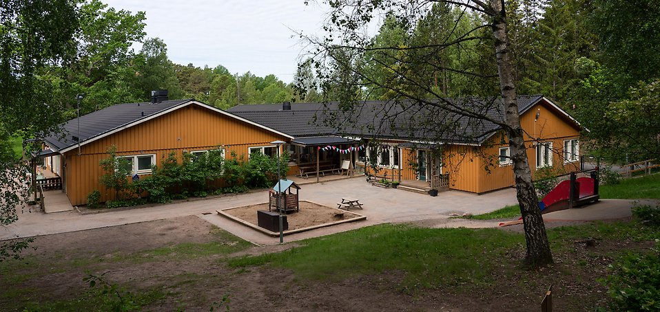 Sjöhästens förskola, gul träbyggnad med sandlåda och gräsbeklädda backar framför