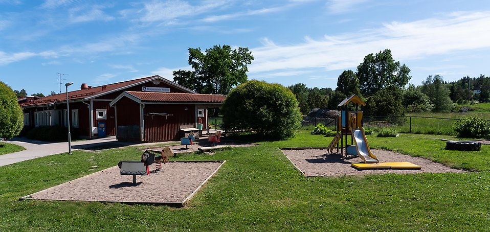 Skärgårdsstads förskola, röd träbyggnad med sandlåda och lekställningar framför