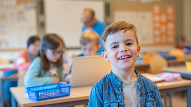 Yngre skolelev ler mot kameran i ett klassrum