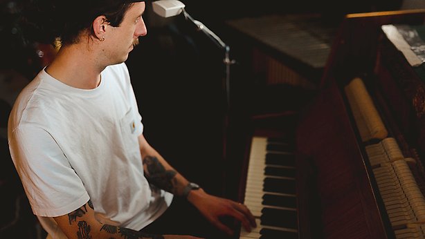Person med vit tröja, tatueringar spelar piano