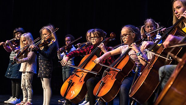 Barn står på en scen och spelar stråkinstrument