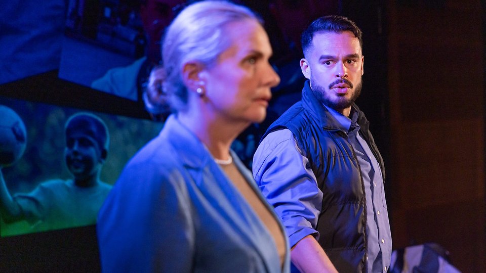 Två personer på en scen, mörk bakgrund.