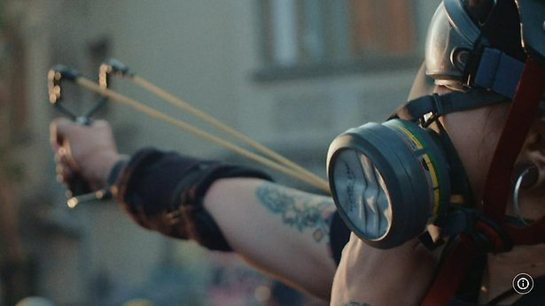 En person i gasmask siktar med slangbella mot okänt mål.