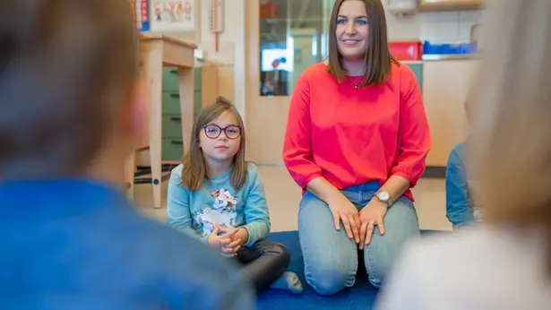 Person sitter bredvid ett barn. I förgrunden finns två bakhuvuden.