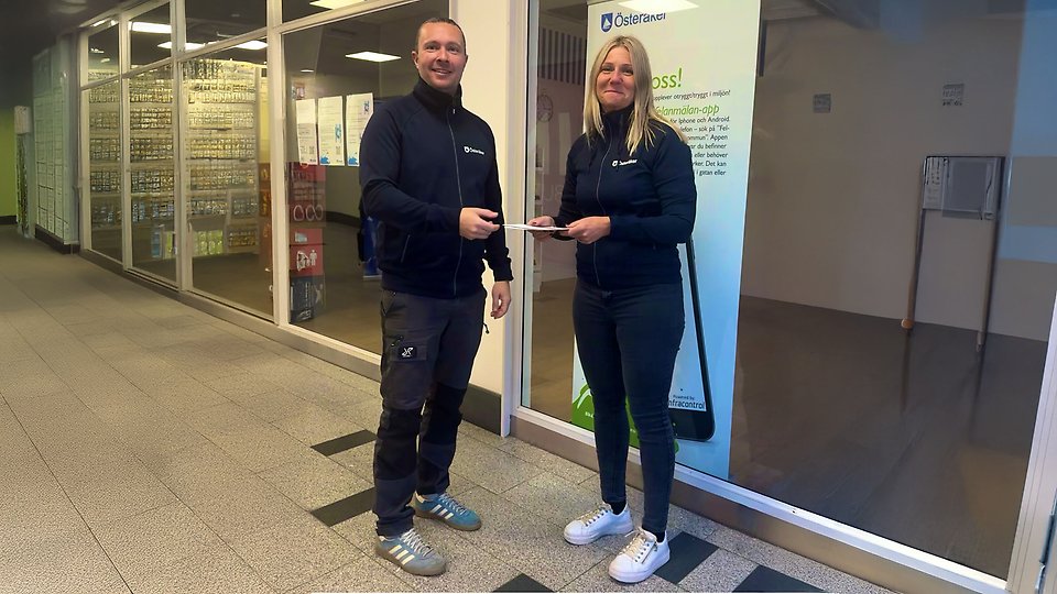 En man och en kvinna står med blåa kläder utanför en lokal i Åkersberga centrum och ser glada ut