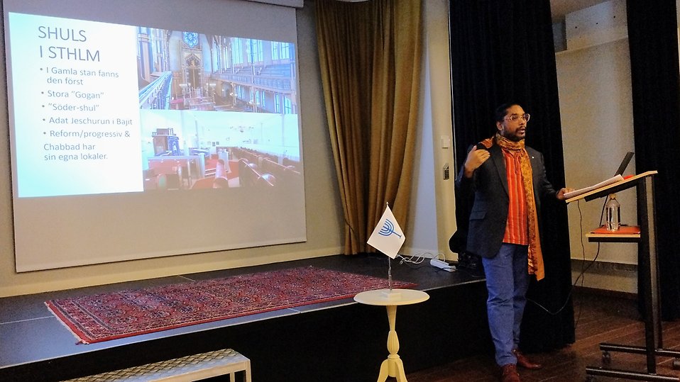 Mikael Gustafsson, lärare vid Paideia folkhögskola, föreläser. Det syns en bild på vita duken om judiska skolor.