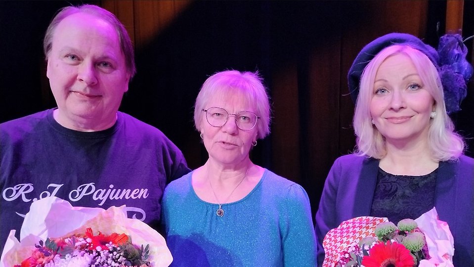 Mies ja nainen ovat saaneet kukkakimpun keskellä seisovalta naishenkilöltä.