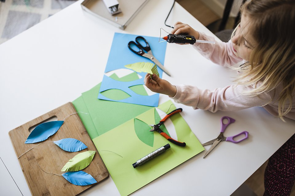 Lapsi istuu värillisten paperiarkkien kanssa ja leikkaa niistä erilaisia puiden lehtien muotoja.