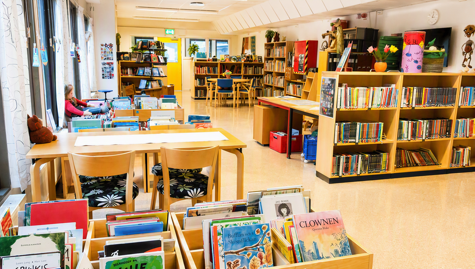 Bild av skolbiblioteket med många böcker i bokhyllor, snurror och fack. Ett ljust rum som inbjuder till läsning i lugn och ro.