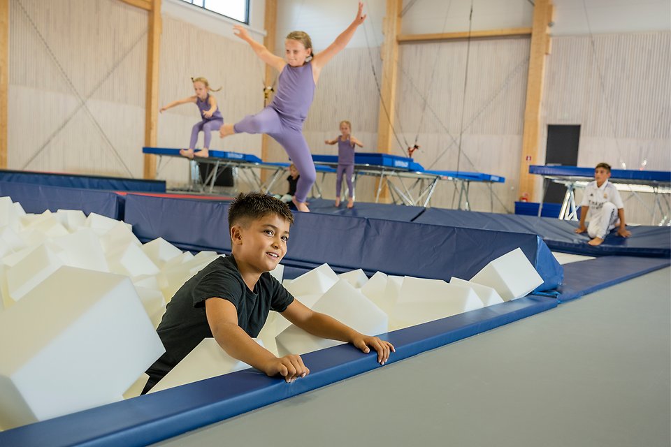 Barn som hoppar på studsmattor och trampoliner ner i en grop fylld med block av skumgummi.