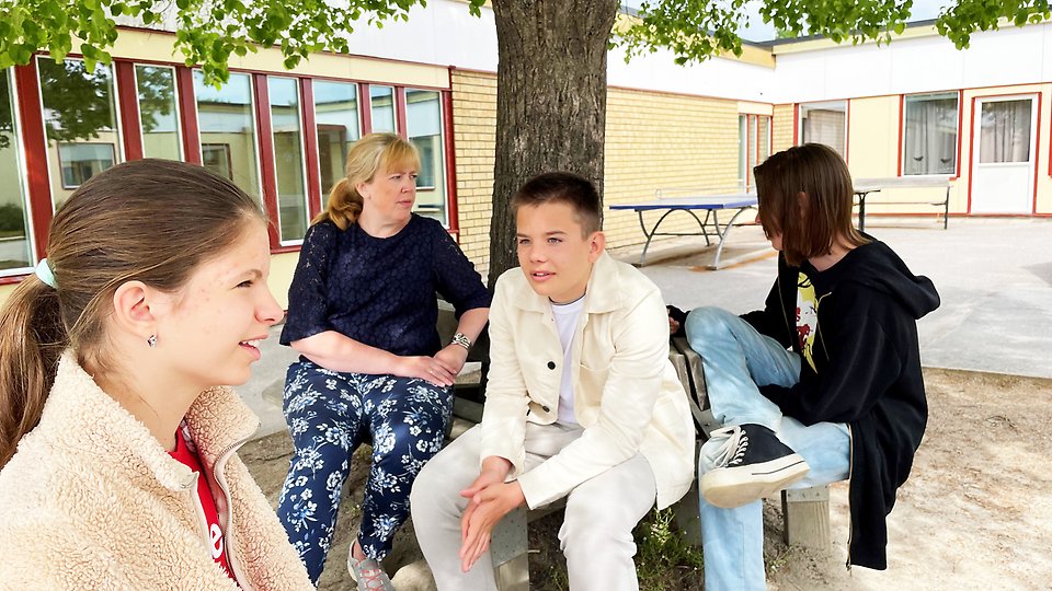 Tre elever och en lärare sitter tillsammans på en skolgård