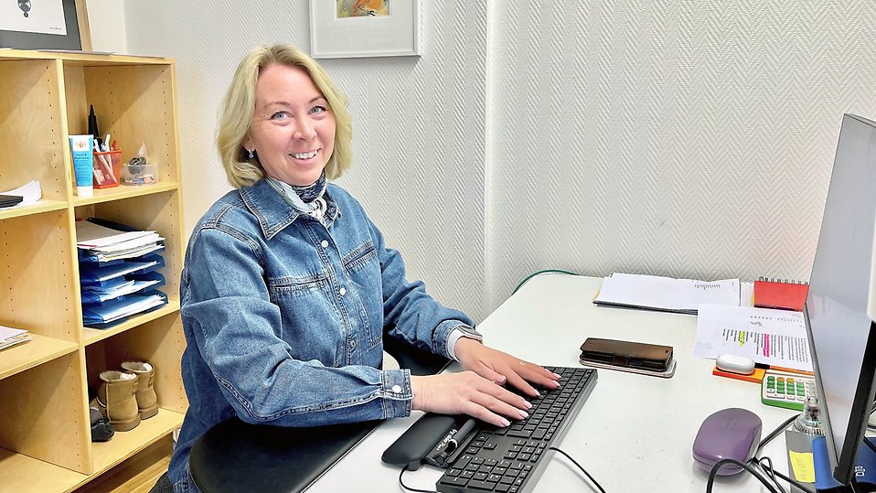 På bilden sitter Jeanette Loo på sitt kontor vid en dator. Hon ler mot kameran och har händerna på tangenbordet.