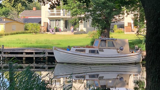 En båt ligger ankrad vid en träbrygga i Åkers kanal. i bakgrunden syns ett hus.
