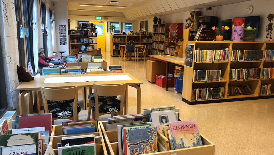 Bild av skolbiblioteket med många böcker i bokhyllor, snurror och fack. Ett ljust rum som inbjuder till läsning i lugn och ro.