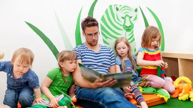 En vuxen man sitter på golvet tillsammans med barn i en förskola och läser en bok.